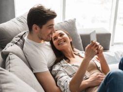 Happy family portrait of positive family lying together on sofa at home and using mobile phone