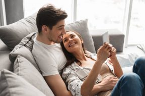 Happy family portrait of positive family lying together on sofa at home and using mobile phone