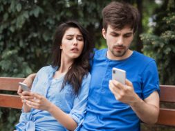 Young couple in the park. Boy is checking his phone hiding it. Girl is lookin into boyfriend's phone with mistrust. What is in your phone concept