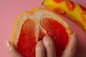 Fingers in grapefruit on pink background. Composition with fresh banana with traces of red lipstick and grapefruit on pink background.