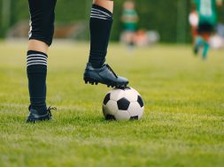 One young football player with ball on grass field. Boy in a sportswear. Player wearing black football socks and soccer cleats. Football horizontal closeup background