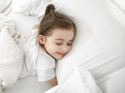 A cute little girl is sleeping in a white bed . Concept of child development and sleep. The view from the top.