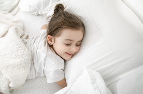 A cute little girl is sleeping in a white bed . Concept of child development and sleep. The view from the top.