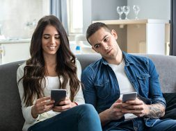 Young couple using smartphones at home. Jealous boyfriend spying his girlfriend's phone.