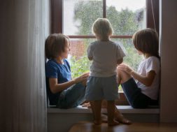 Happy siblings, boy brothers, sitting on a window shield on a rainy day, playing together, summertime