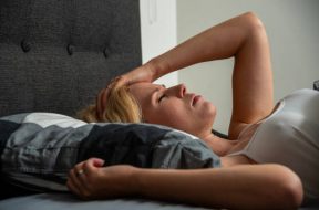 Blond Woman can't sleep at night because of her problems. One hand holding her for-head
