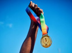 Raised hand holding a gold medal against blue sky. Victory and achievement concept.