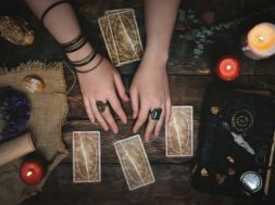 Tarot cards, magic book and fortune teller hands on a wooden table background. Future reading concept. Divination.