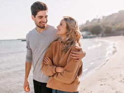 Pleasant young man embracing girlfriend on nature background. Outdoor photo of pleased blonde girl posing at sea with husband.